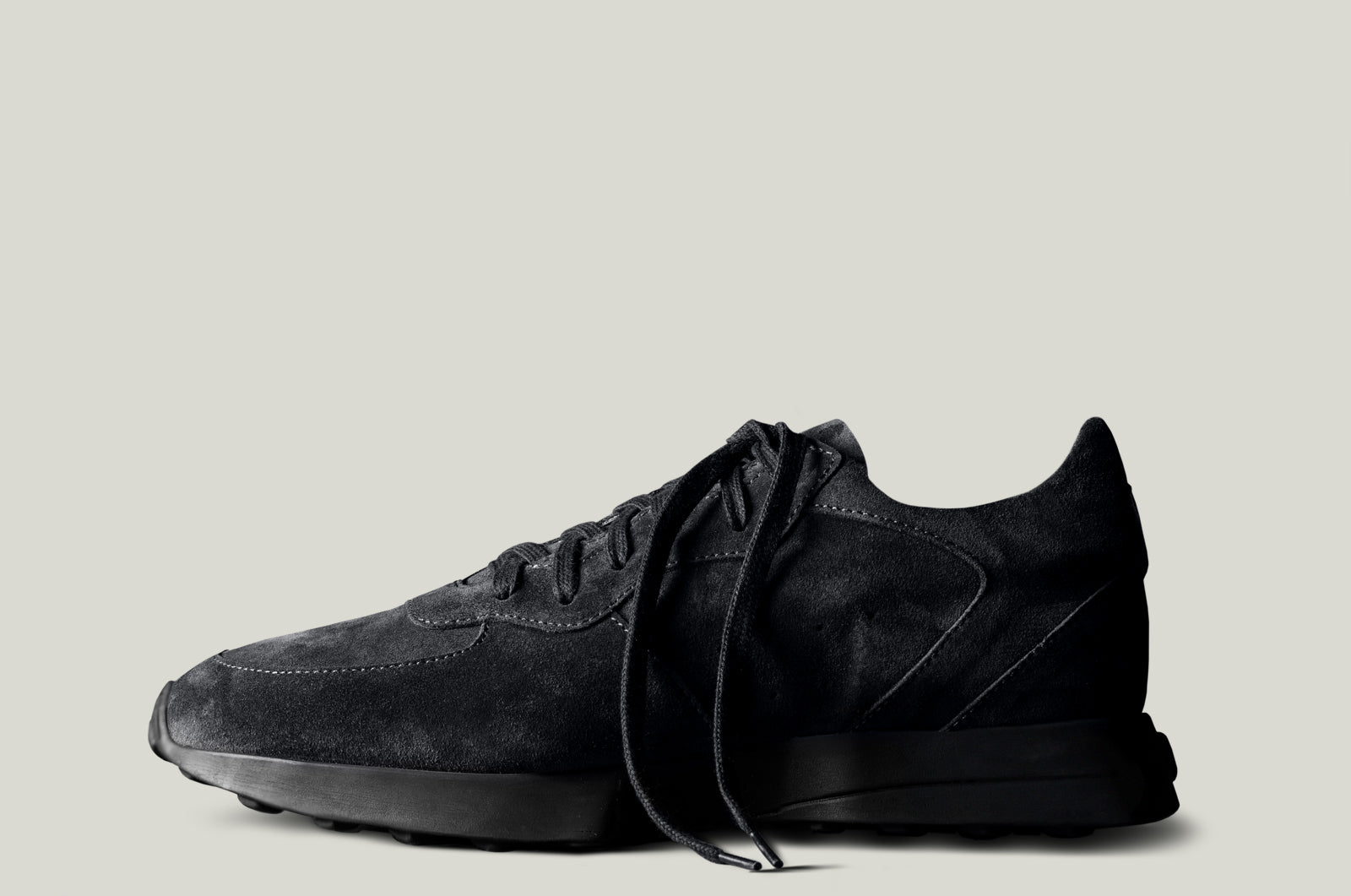 A single black suede sneaker with laces, set against a white background.