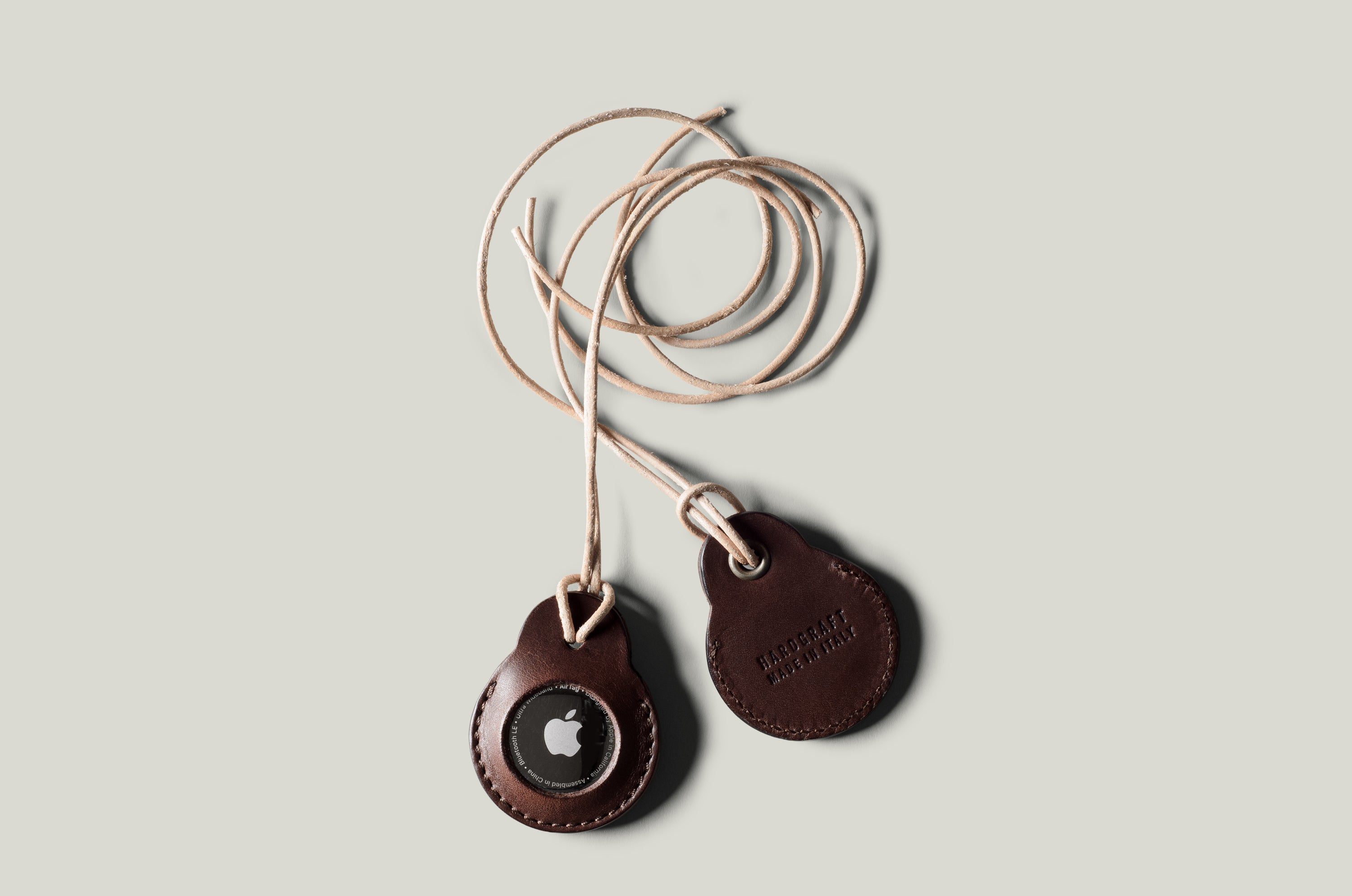 A pair of dark brown apple airtag holders on a light grey background