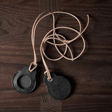 A pair of black leather Apple airtag holders on wood background