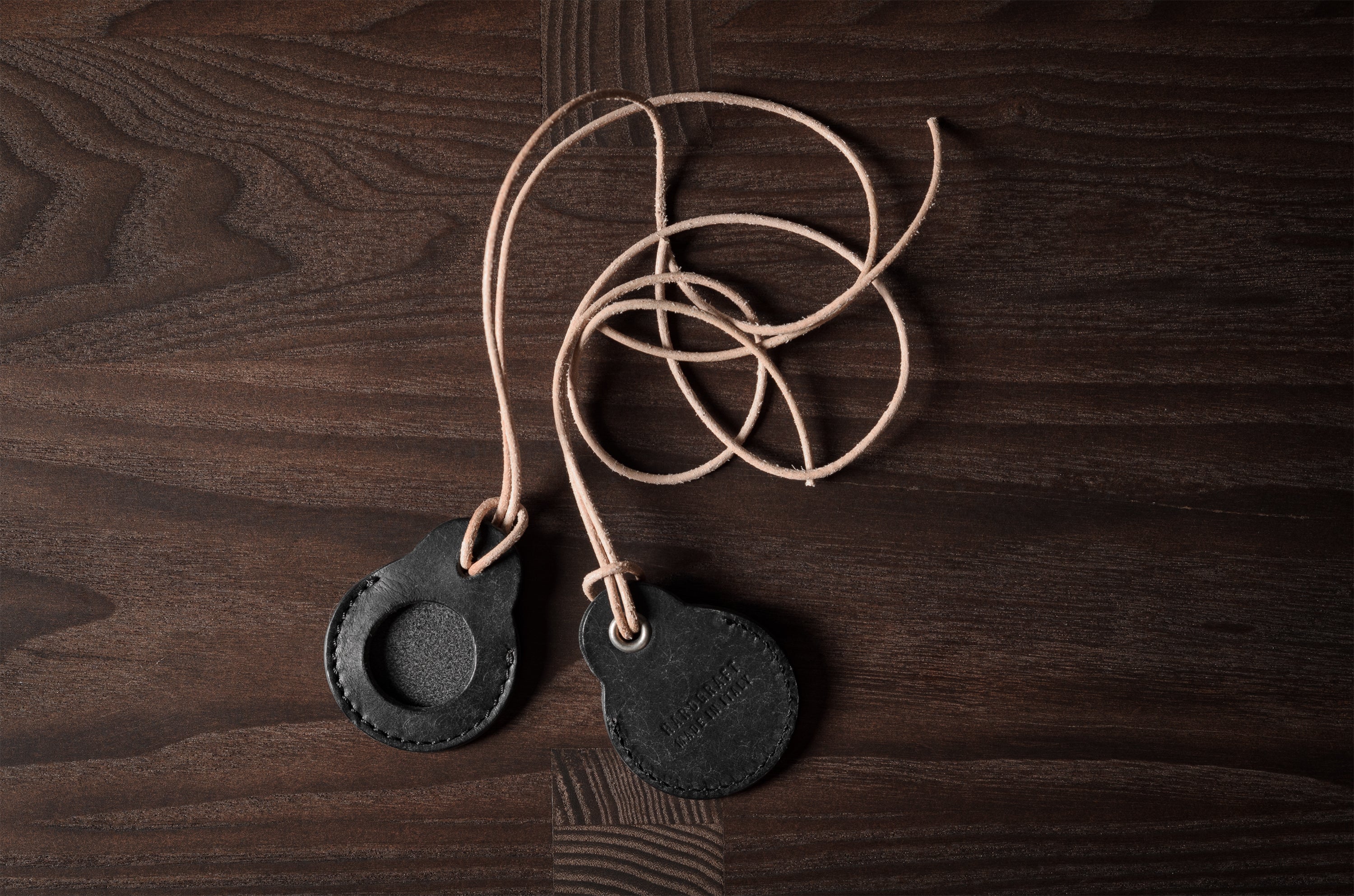 A pair of black leather Apple airtag holders on wood background