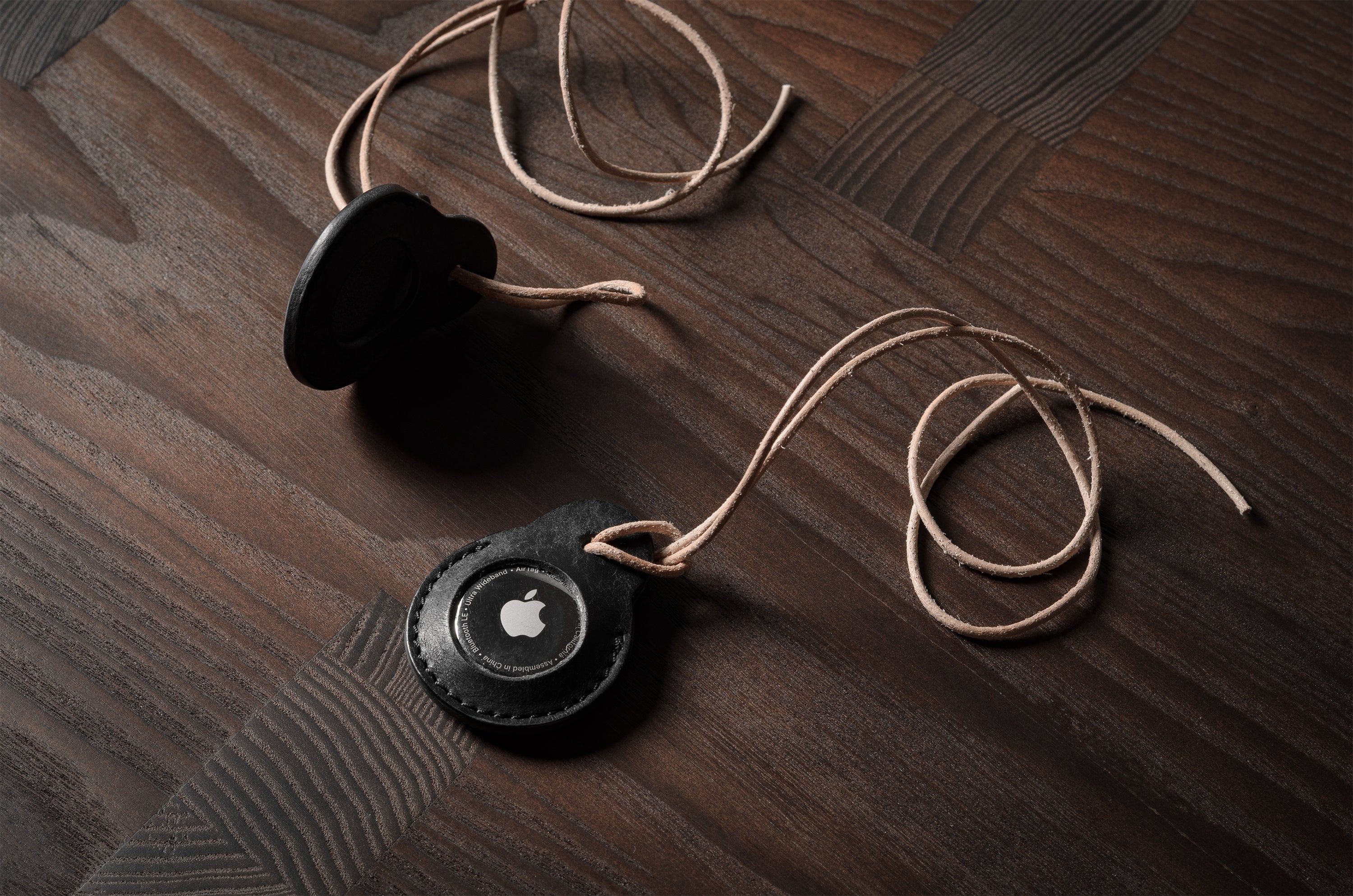 A pair of black leather Apple airtag holders on wood background