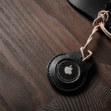 A pair of black leather Apple airtag holders on wood background
