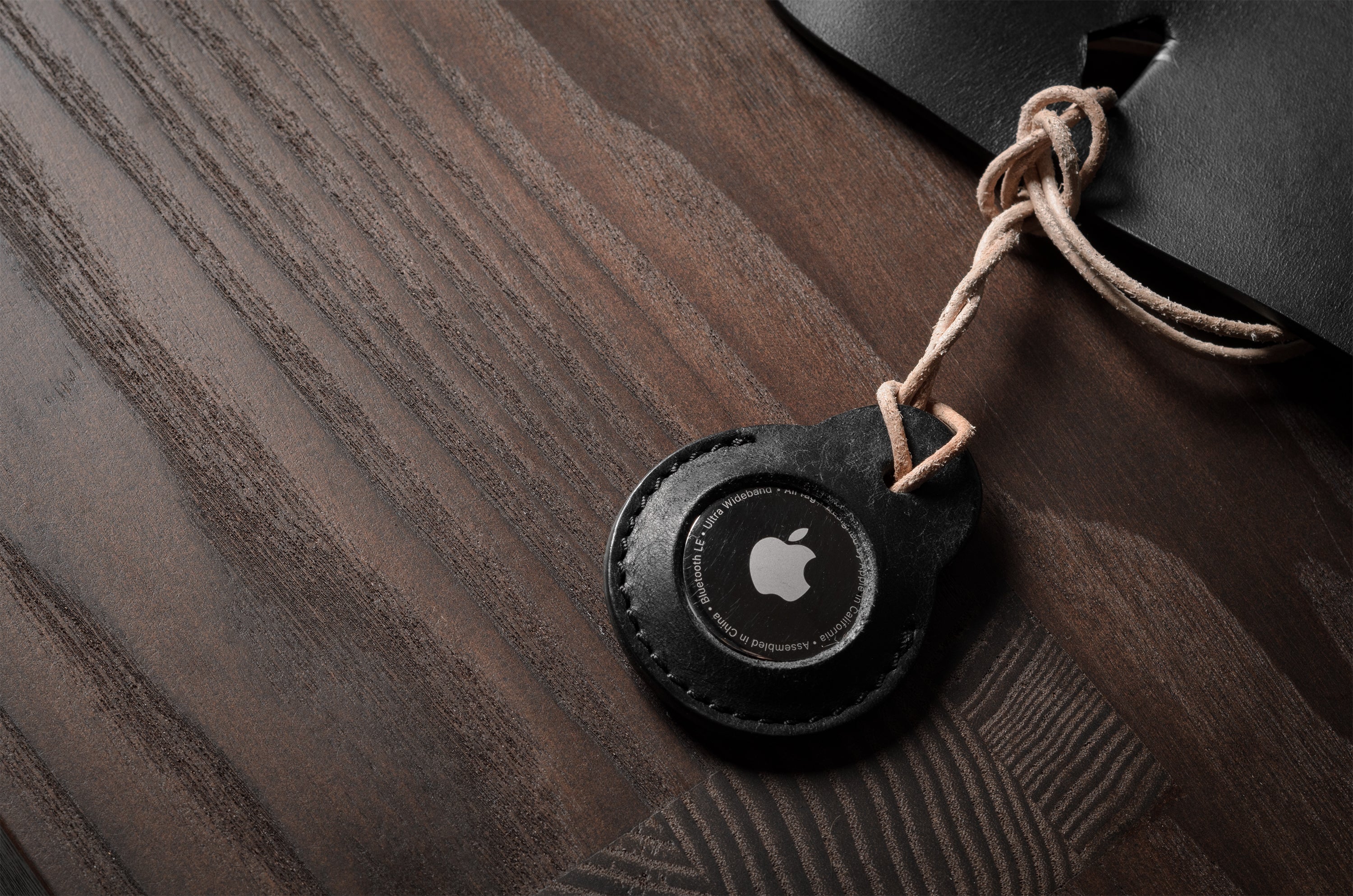 A pair of black leather Apple airtag holders on wood background