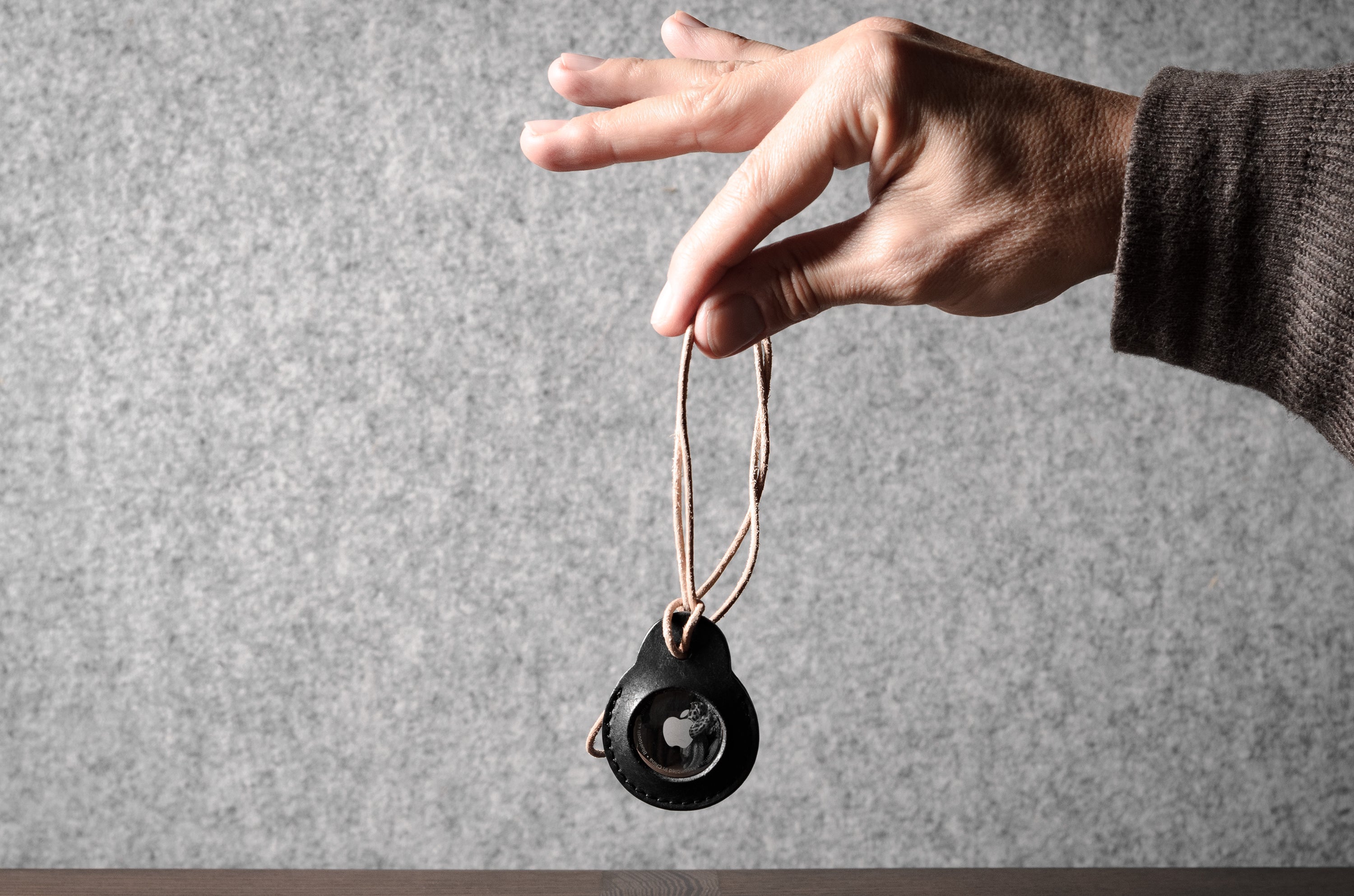 A pair of black leather Apple airtag holders held by a hand