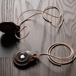 A pair of dark brown apple airtag holders on a wood background