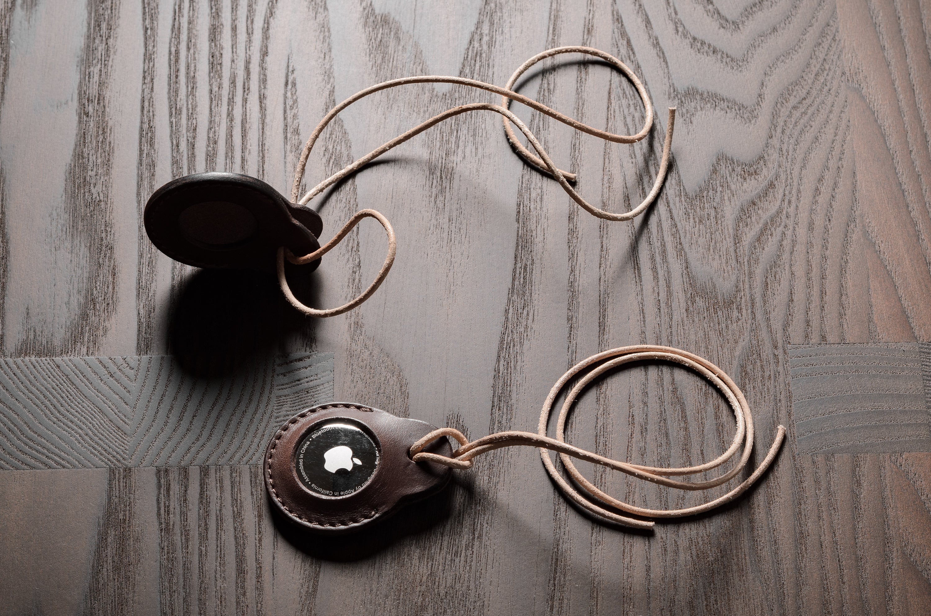 A pair of dark brown apple airtag holders on a wood background