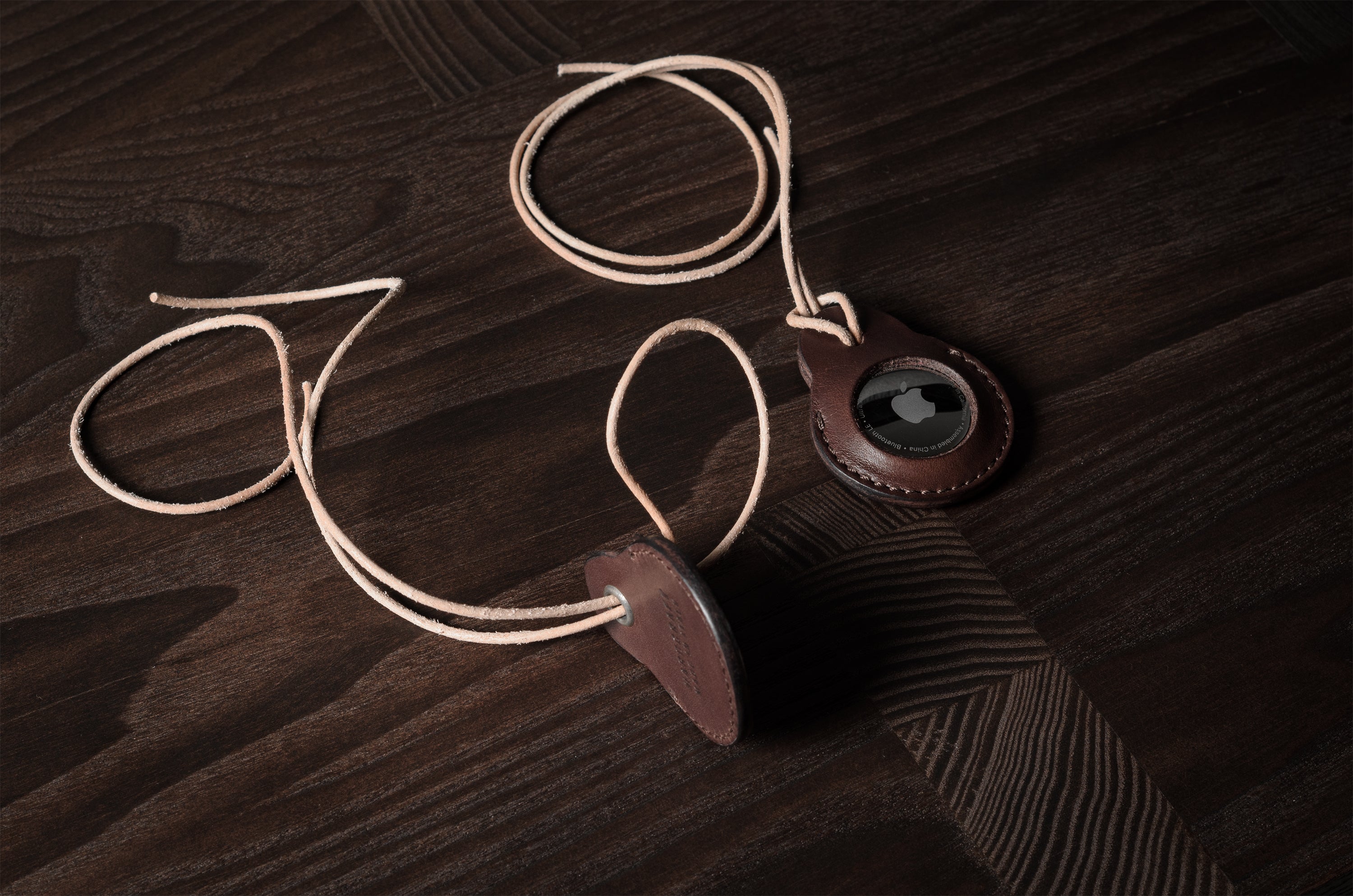 A pair of dark brown apple airtag holders on a wood background