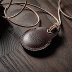 A pair of dark brown apple airtag holders on a wood background