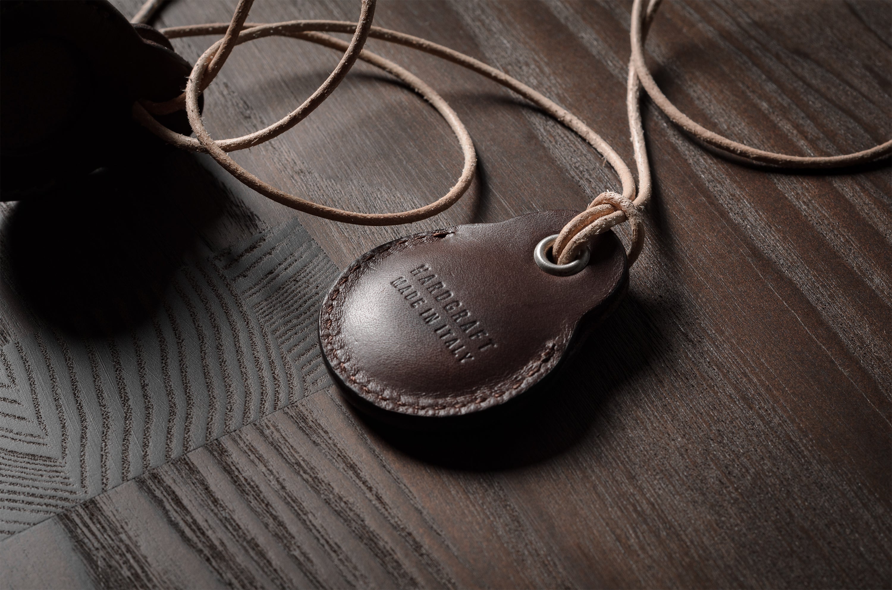 A pair of dark brown apple airtag holders on a wood background