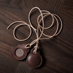 A pair of dark brown apple airtag holders on a wood background