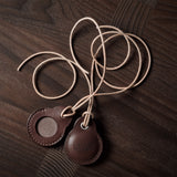 A pair of dark brown apple airtag holders on a wood background