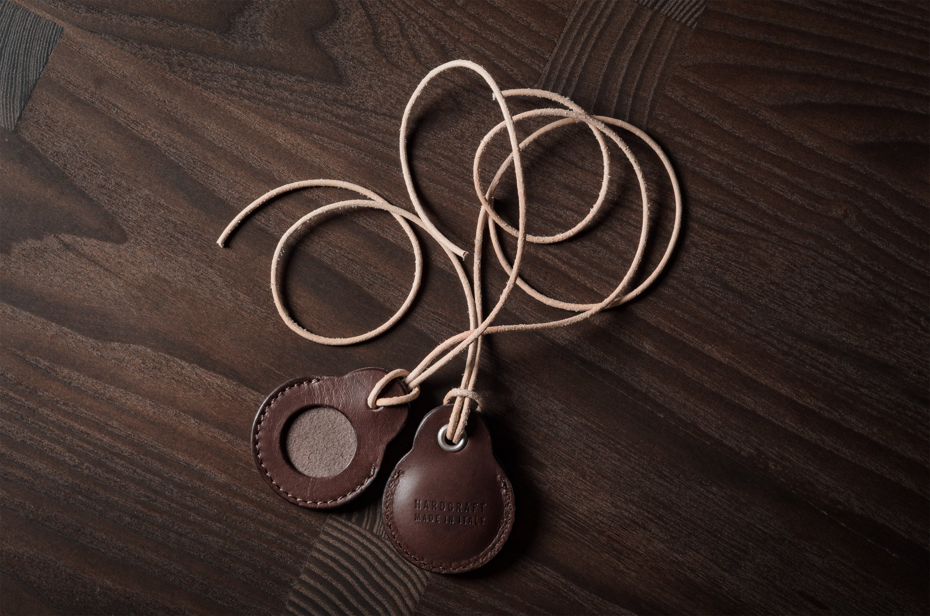 A pair of dark brown apple airtag holders on a wood background