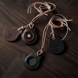 A pair of dark brown  and black apple airtag holders on a wood background