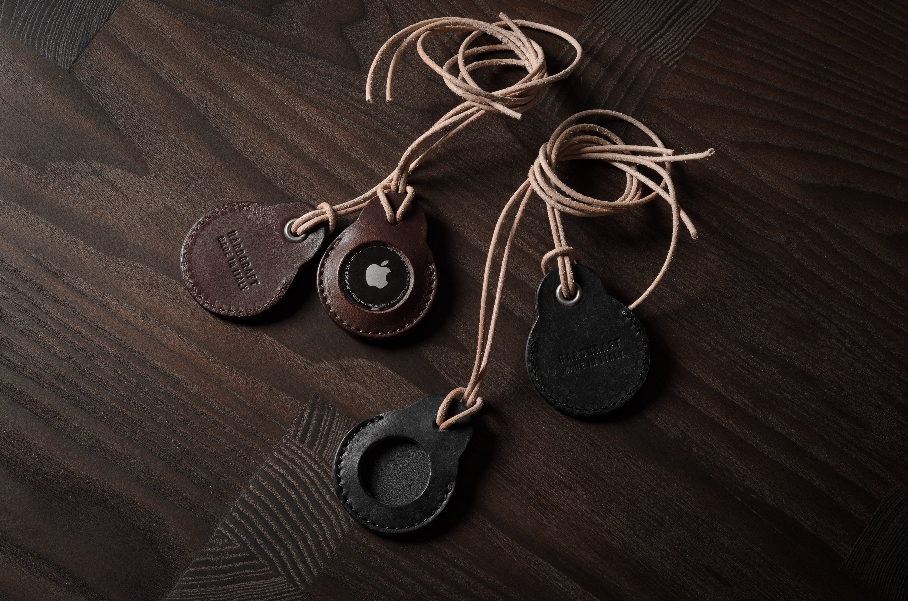 A pair of dark brown  and black apple airtag holders on a wood background