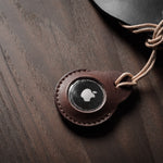A pair of dark brown apple airtag holders on a wood background