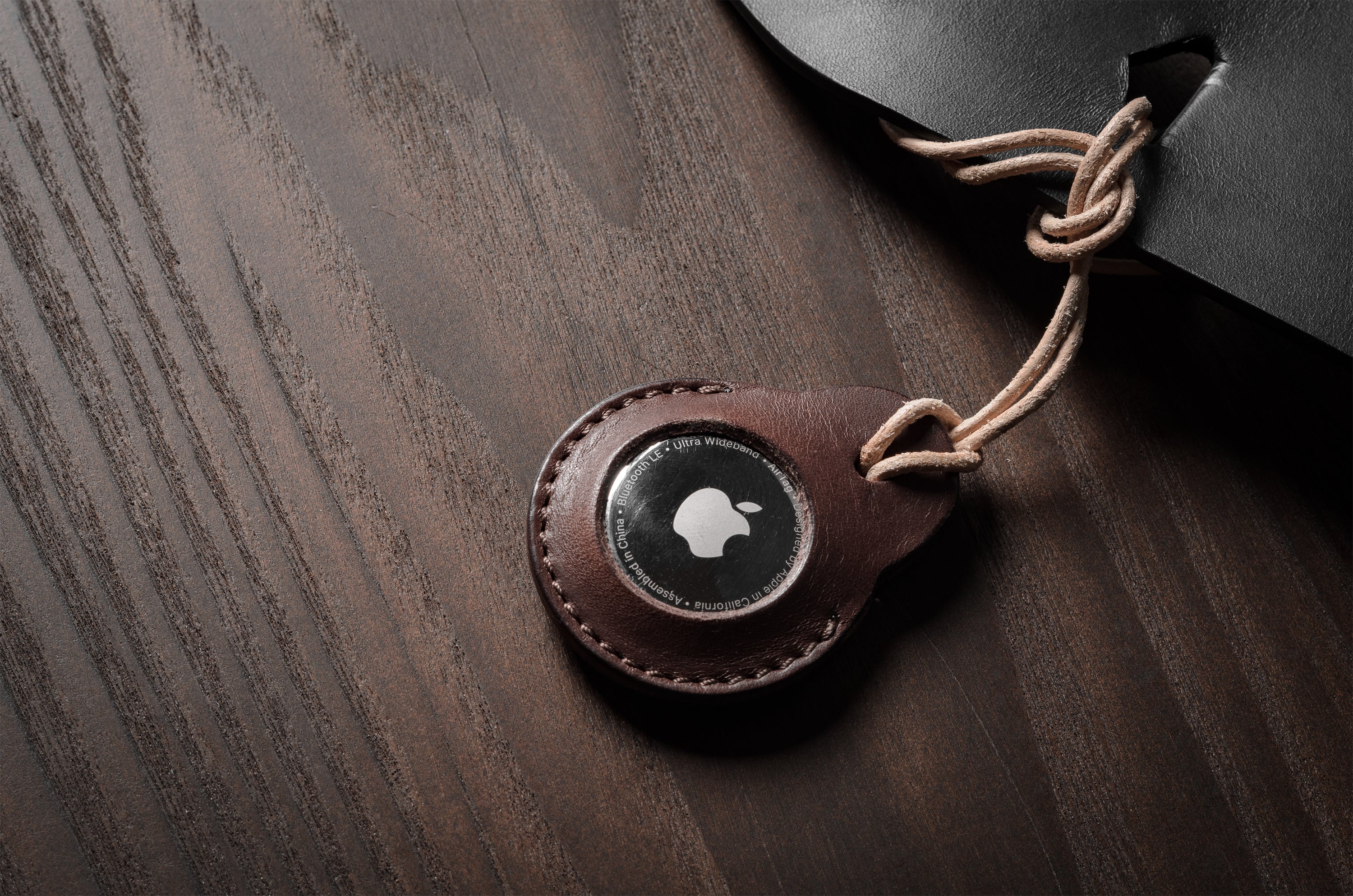 A pair of dark brown apple airtag holders on a wood background