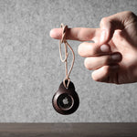 A pair of dark brown apple airtag holders held by a hand