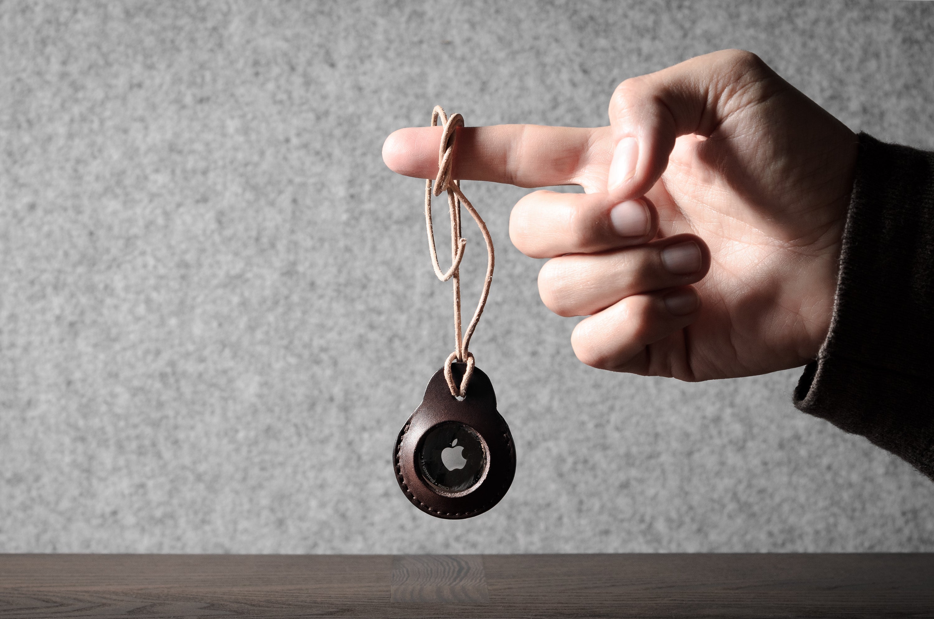 A pair of dark brown apple airtag holders held by a hand