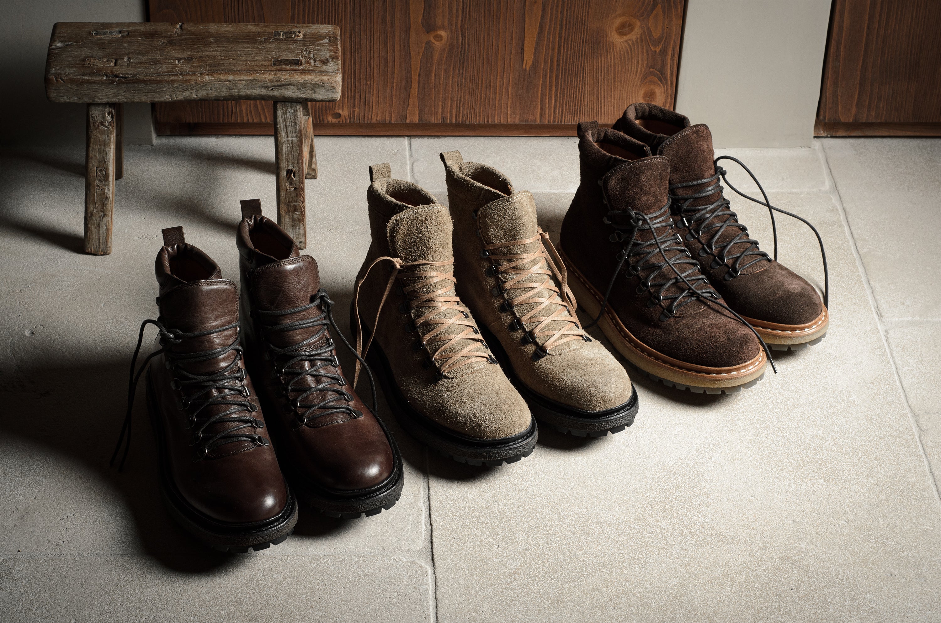 Set of brown and beige boots on a concrete floor with a wooden bench in the background.