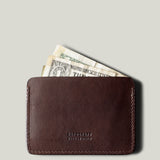 Brown leather card case with money on a light gray background