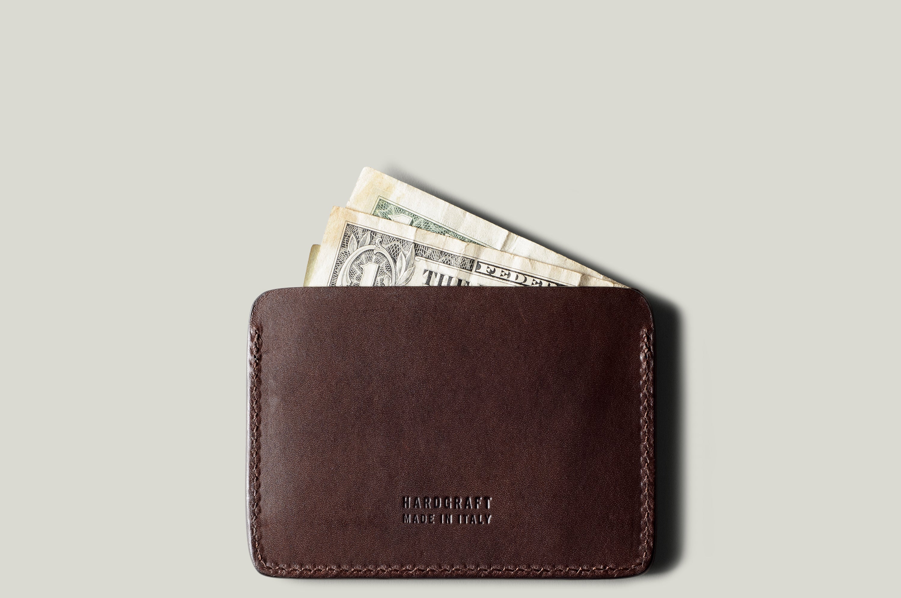 Brown leather card case with money on a light gray background