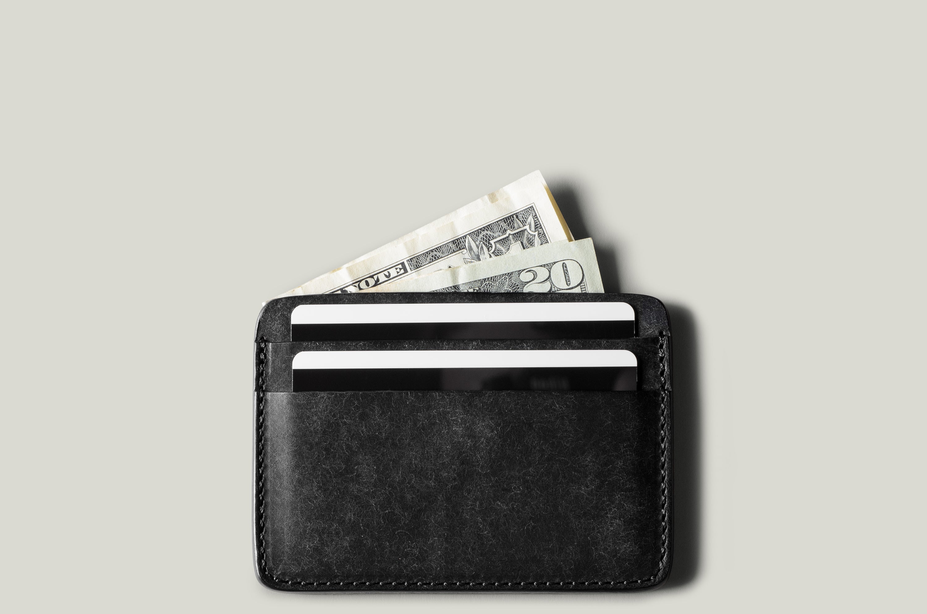 Black card case with money and cards on a light gray background