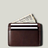 Brown leather card case with money and cards on a light gray background
