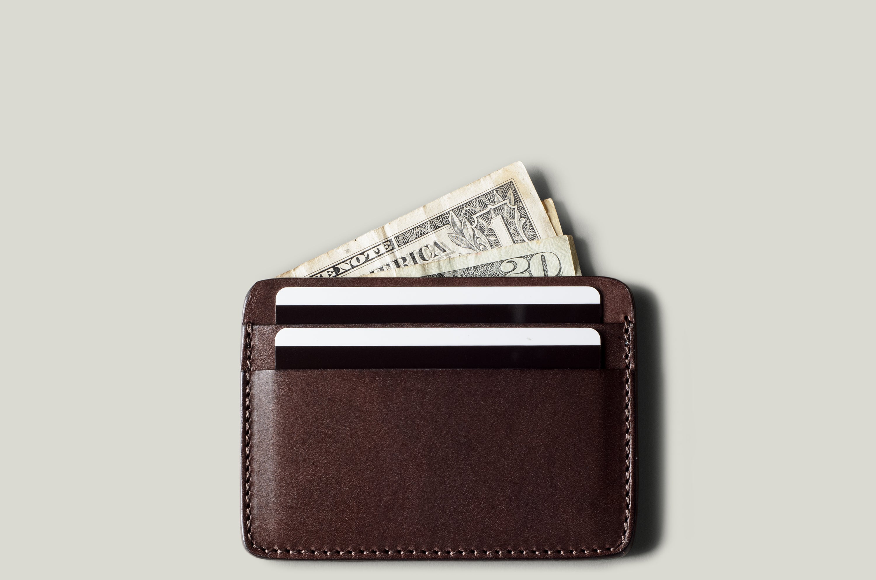 Brown leather card case with money and cards on a light gray background