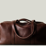 Brown leather duffel bag on a light beige background