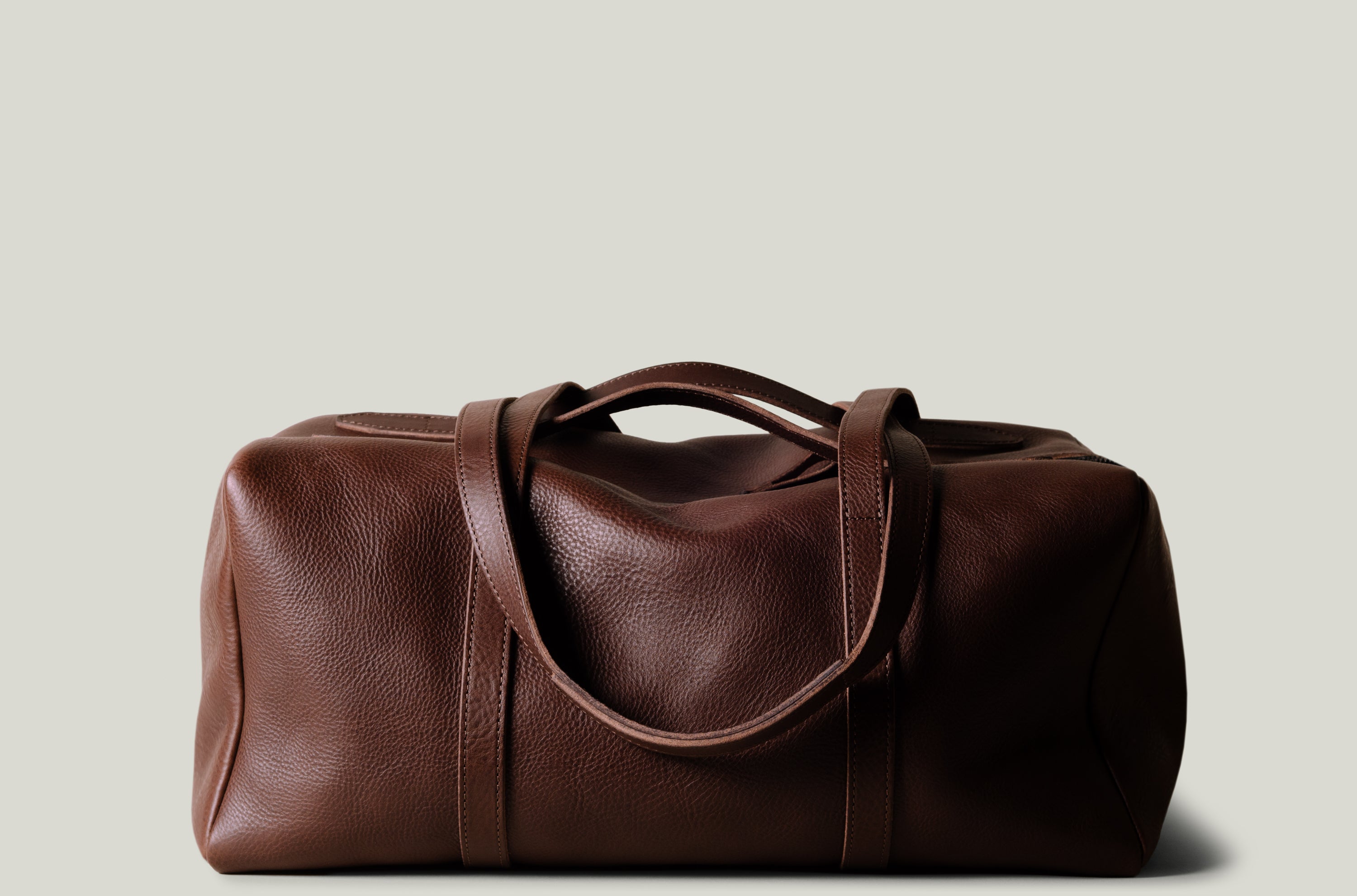 Brown leather duffel bag on a light beige background