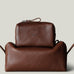 Two brown pebbled leather toiletry bags stacked together on a light gray background. The smaller rectangular zip pouch sits on top of a larger pouch.
