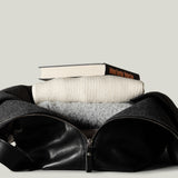 Black leather duffel bag with books inside on a light gray background