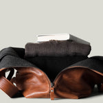 Brown leather bag with a brown sweater and book on a light gray background