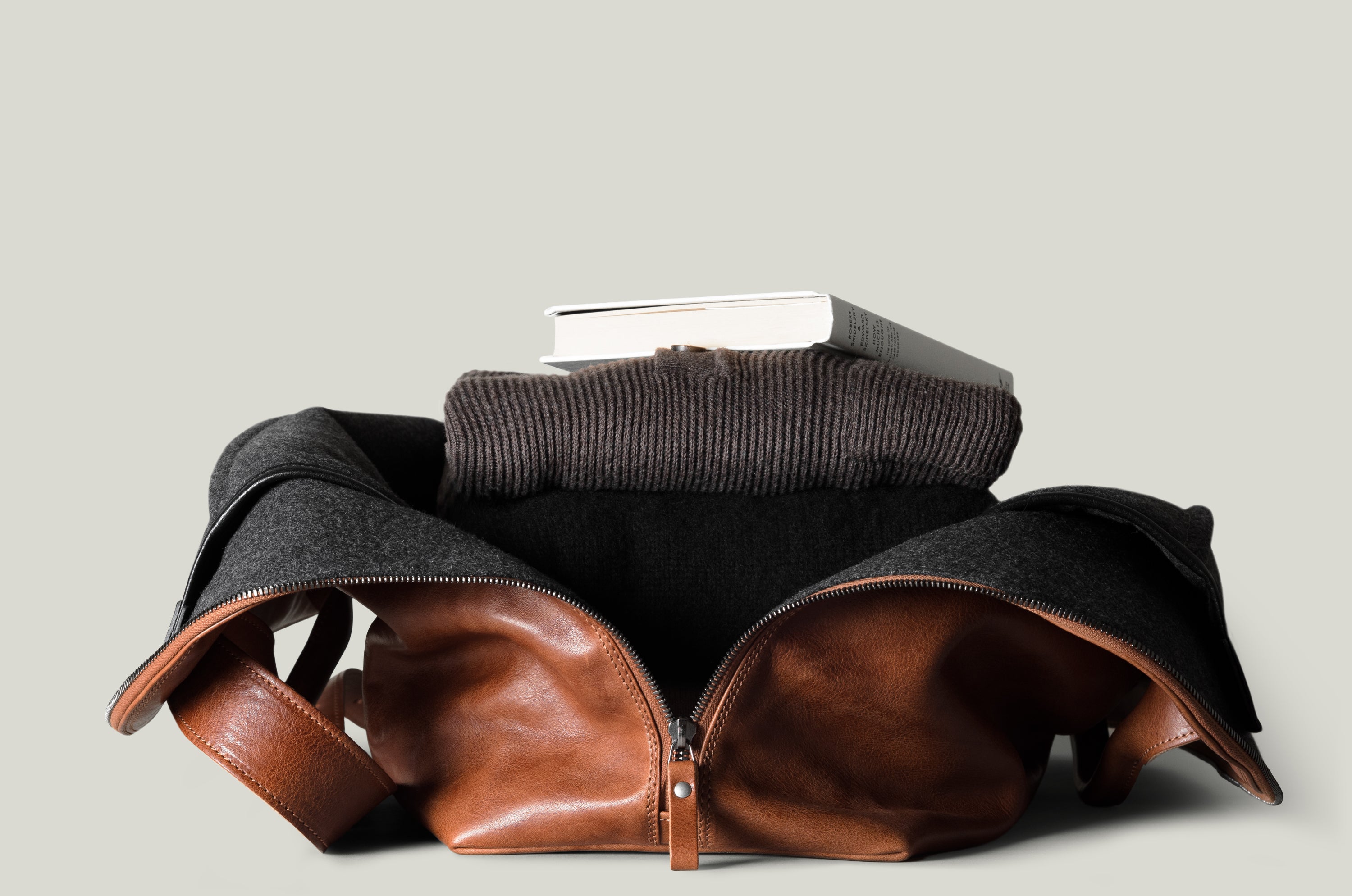 Brown leather bag with a brown sweater and book on a light gray background