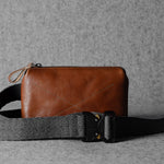 Brown leather bag with a black strap on a gray background