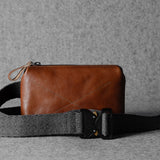 Brown leather bag with a black strap on a gray background