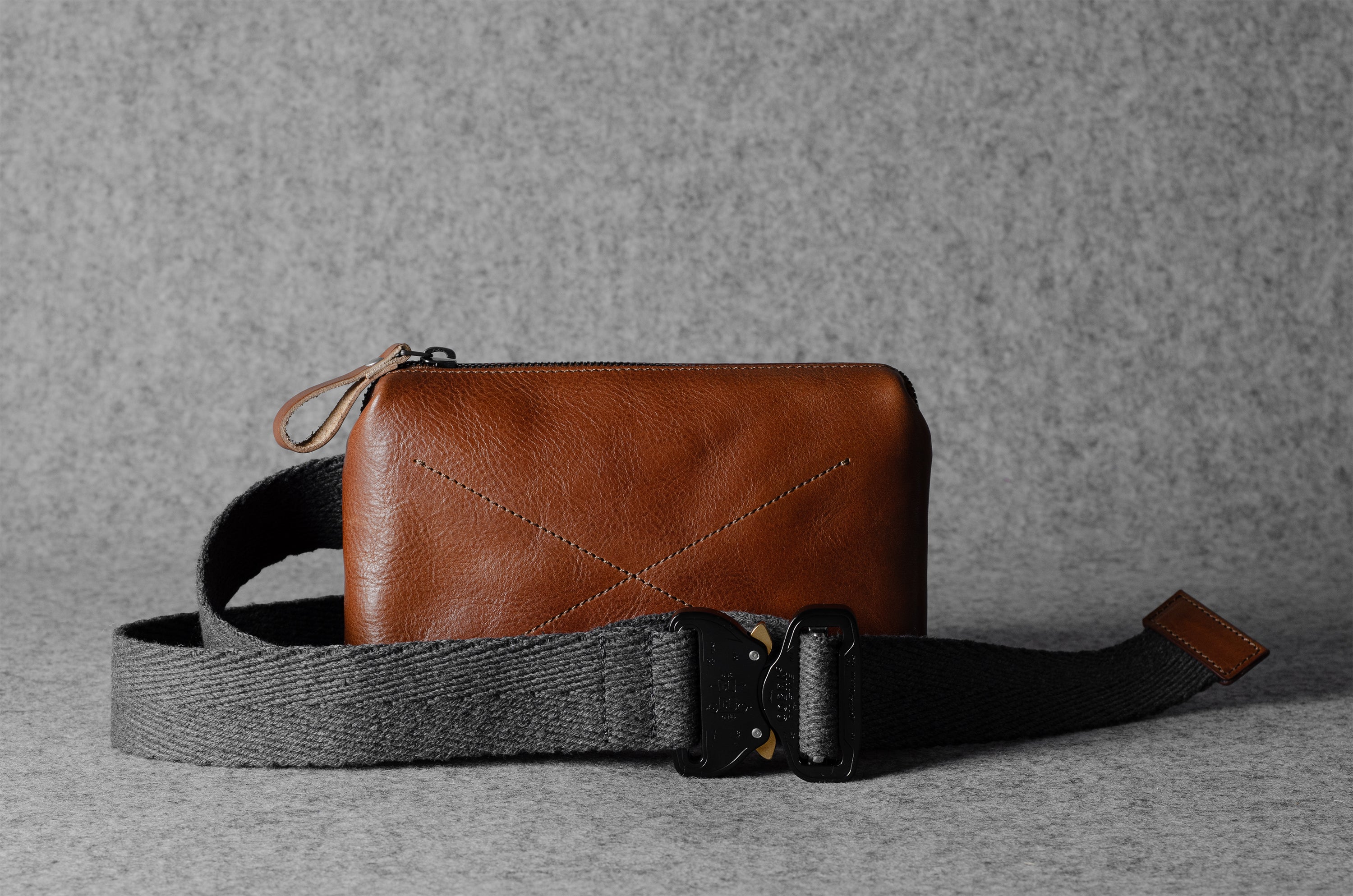 Brown leather bag with a black strap on a gray background