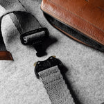 Brown leather crossbody bag with a gray strap on a gray background