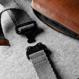Brown leather crossbody bag with a gray strap on a gray background