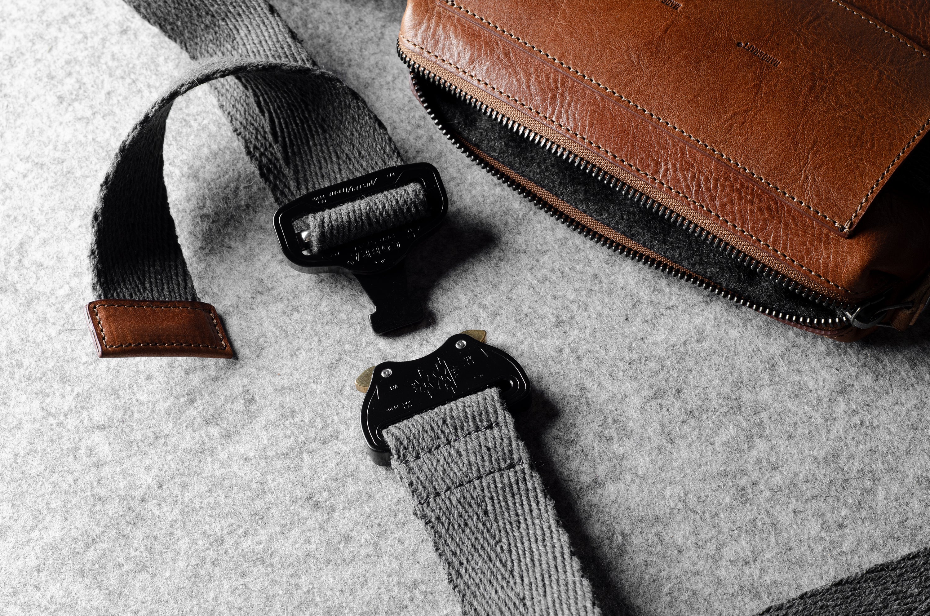 Brown leather crossbody bag with a gray strap on a gray background