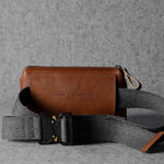 Brown leather crossbody bag with a gray strap on a gray background