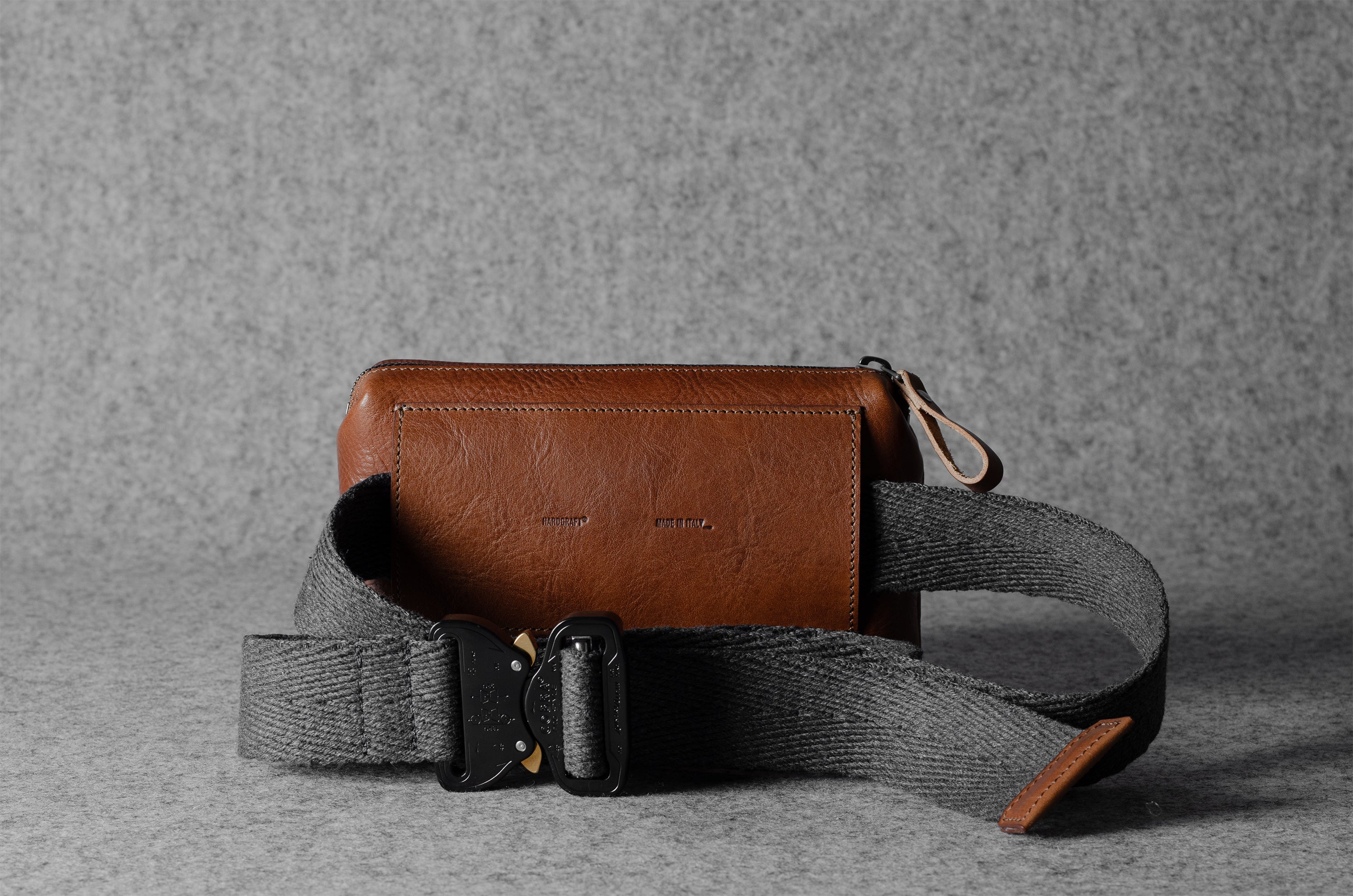 Brown leather crossbody bag with a gray strap on a gray background