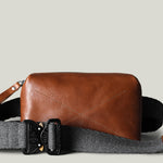 Brown leather crossbody bag with gray strap on a beige background