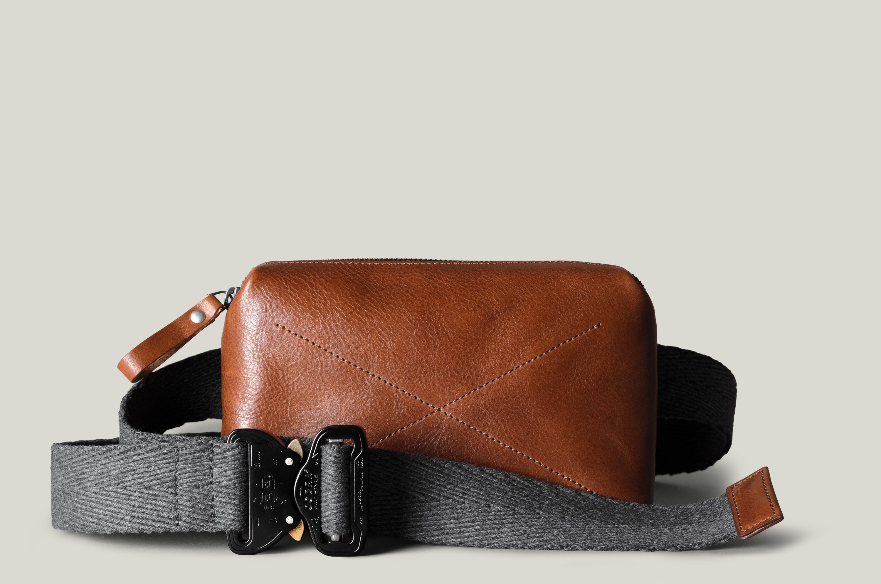 Brown leather crossbody bag with gray strap on a beige background