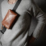 Person wearing a brown leather crossbody bag against a dark background