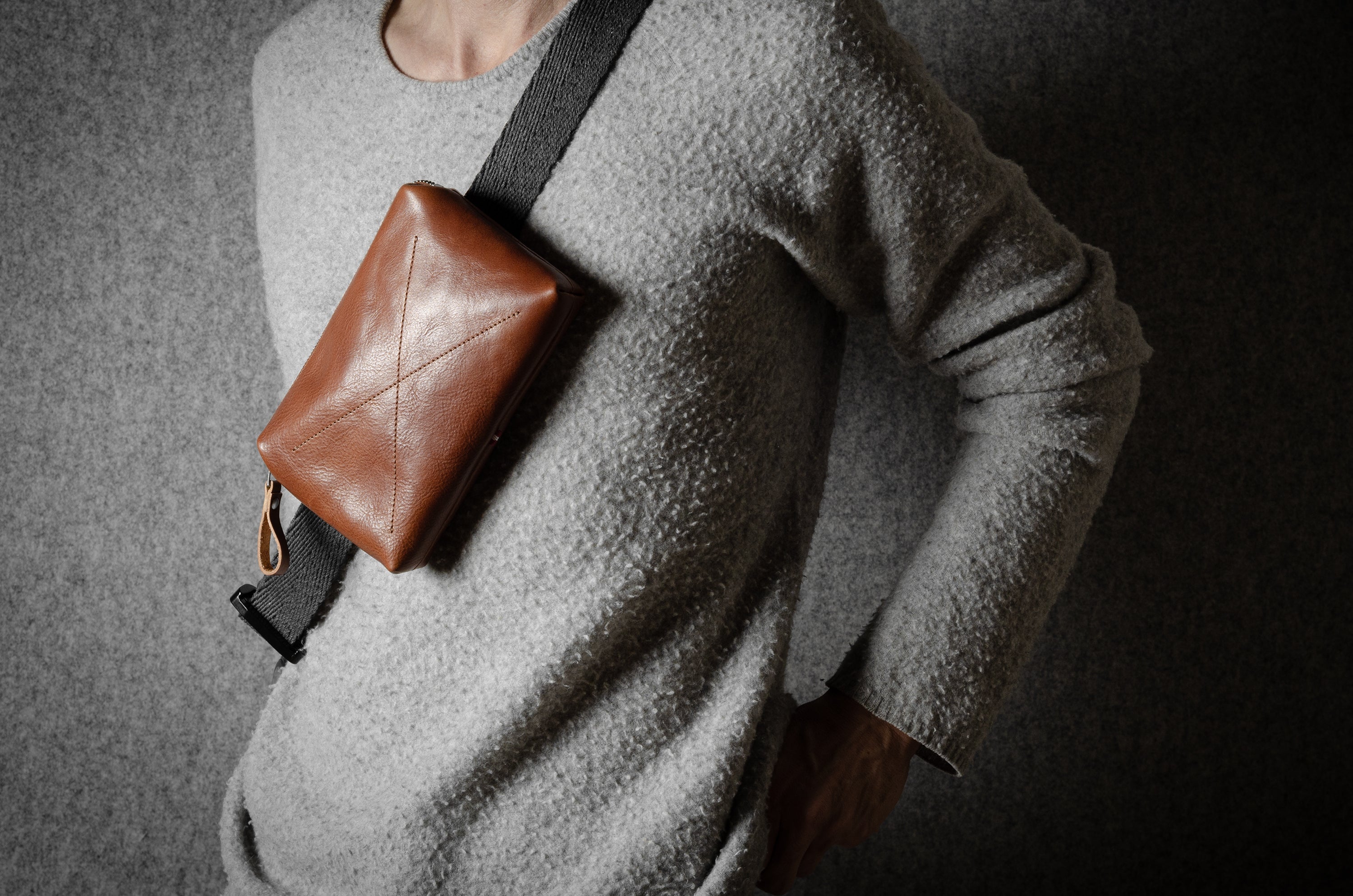 Person wearing a brown leather crossbody bag against a dark background