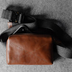 Brown leather pouch with a black strap on a gray surface