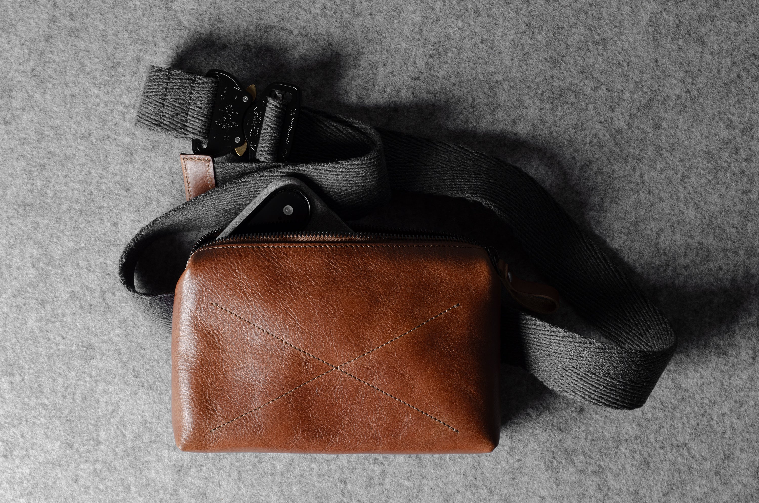 Brown leather pouch with a black strap on a gray surface