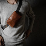 Person wearing a brown leather crossbody bag with a dark background