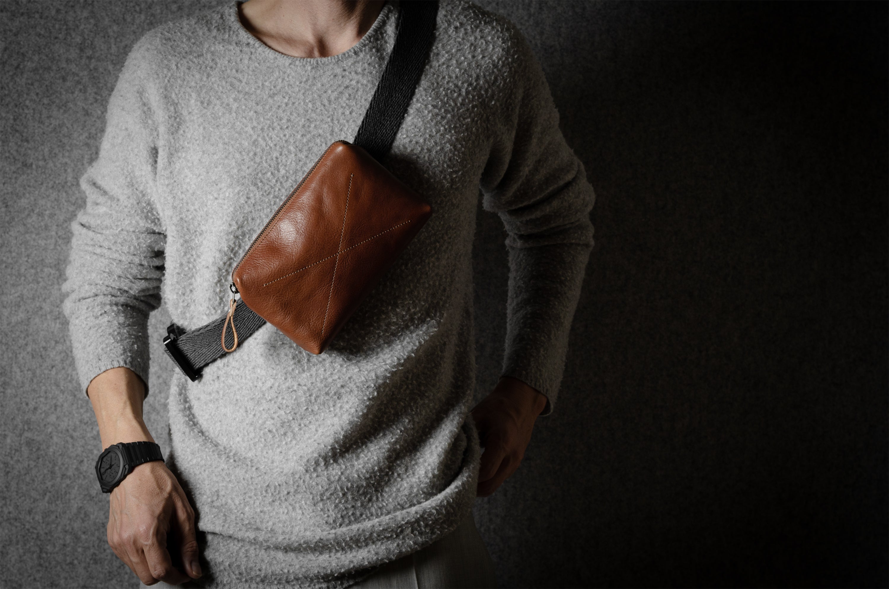 Person wearing a brown leather crossbody bag with a dark background